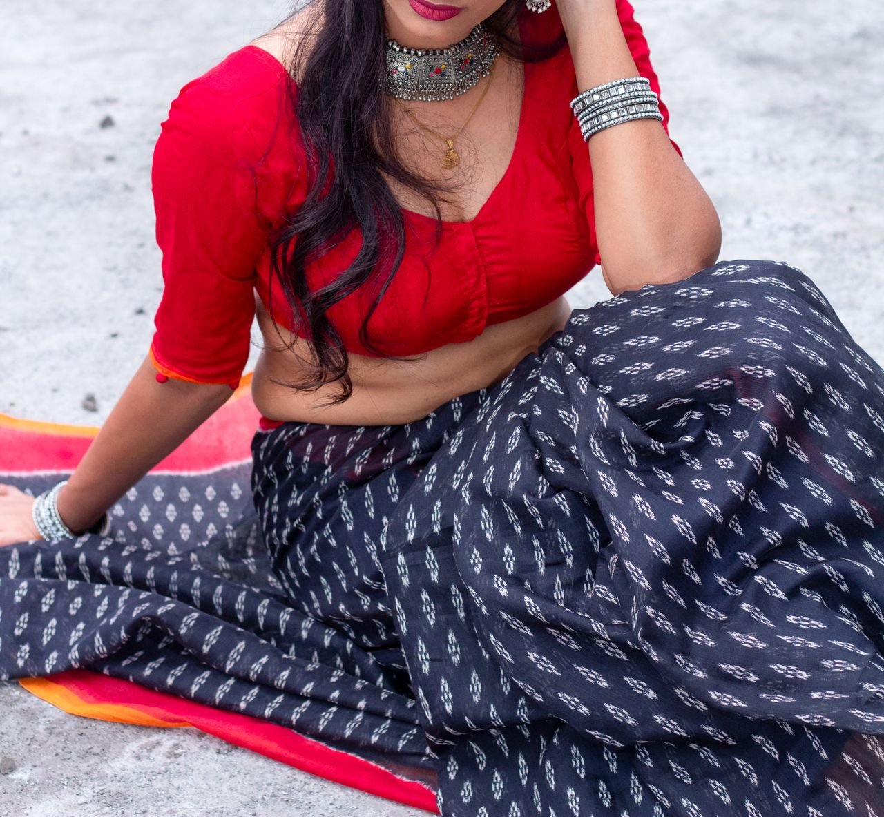 Woman in a vibrant red blouse and patterned saree, showcasing traditional Indian attire and jewelry.